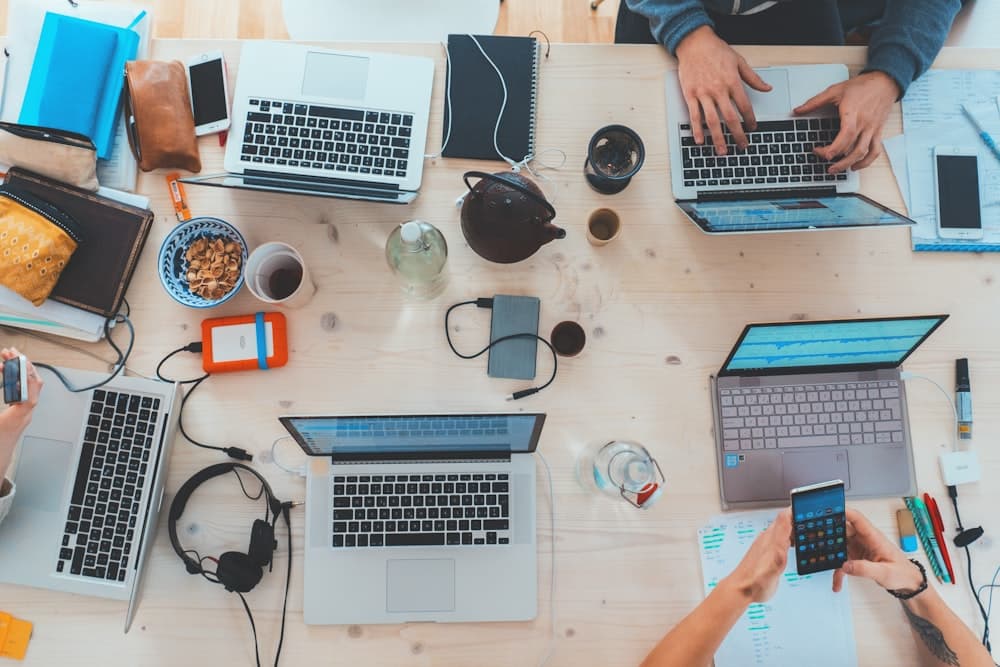 Top-down view of a busy desk with laptops, notes, and a phone